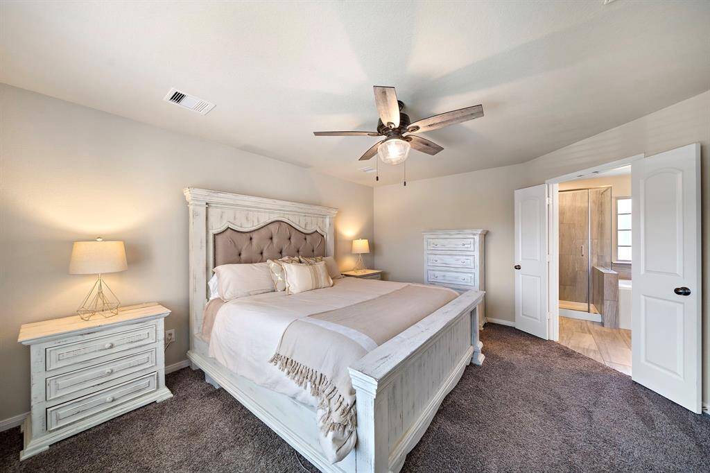 Retreat to the spacious primary bedroom, featuring plush carpet flooring, a tray ceiling with modern fan, and elegant neutral tones creating a peaceful atmosphere. Enjoy direct access to the luxurious ensuite bath with dual sinks, a glass-enclosed shower, and a relaxing soaking tub—designed for ultimate comfort and convenience.