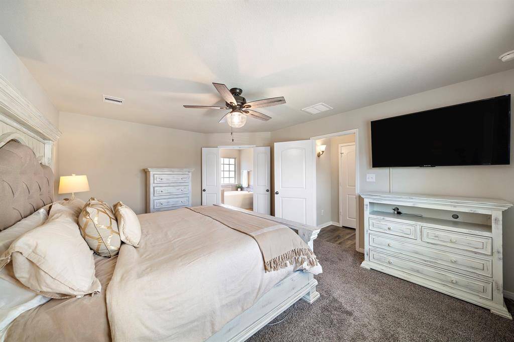The primary bedroom offers a tranquil retreat, featuring plush carpeting, neutral tones, and a beautiful tray ceiling with modern fan. Spacious enough for a king bed and large furnishings, this suite enjoys direct access to the luxurious ensuite bath with soaking tub and dual vanities.