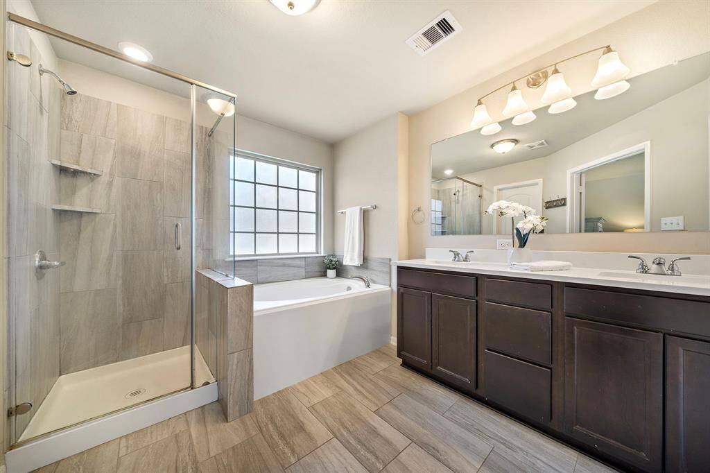 Enjoy spa-inspired relaxation in the primary ensuite bath, featuring a crisp dual sink vanity, glass-enclosed shower, and generously sized soaking tub beneath a privacy window. Tile floors, abundant counter space, and elegant fixtures create a tranquil oasis designed for both style and everyday comfort.