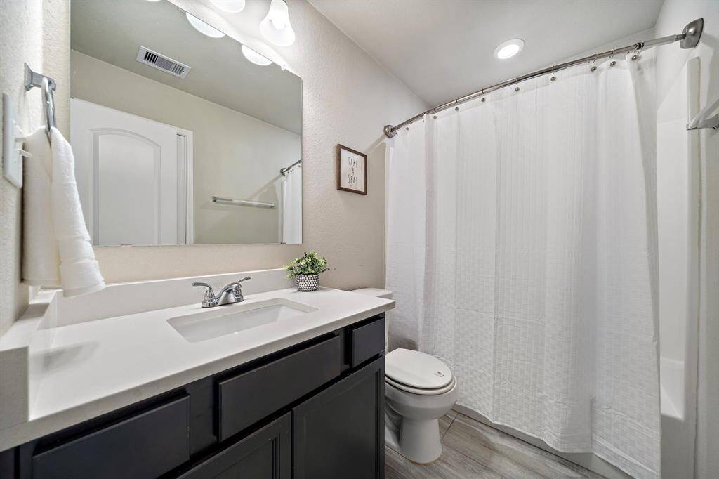 Sleek secondary bath offers a spacious vanity with quartz countertop, modern fixtures, and a convenient tub/shower combo behind a full-length curtain. Contemporary tile flooring and neutral tones provide both style and easy-care practicality for daily routines.