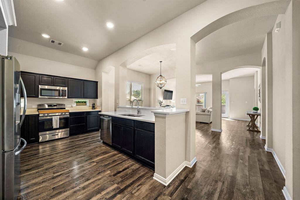 Sleek kitchen features abundant cabinet space, quartz countertops, a breakfast bar, and stainless steel appliances including a gas range. Modern backsplash and a spacious dual sink enhance functionality, while the open layout connects seamlessly to the adjacent dining and living areas.
