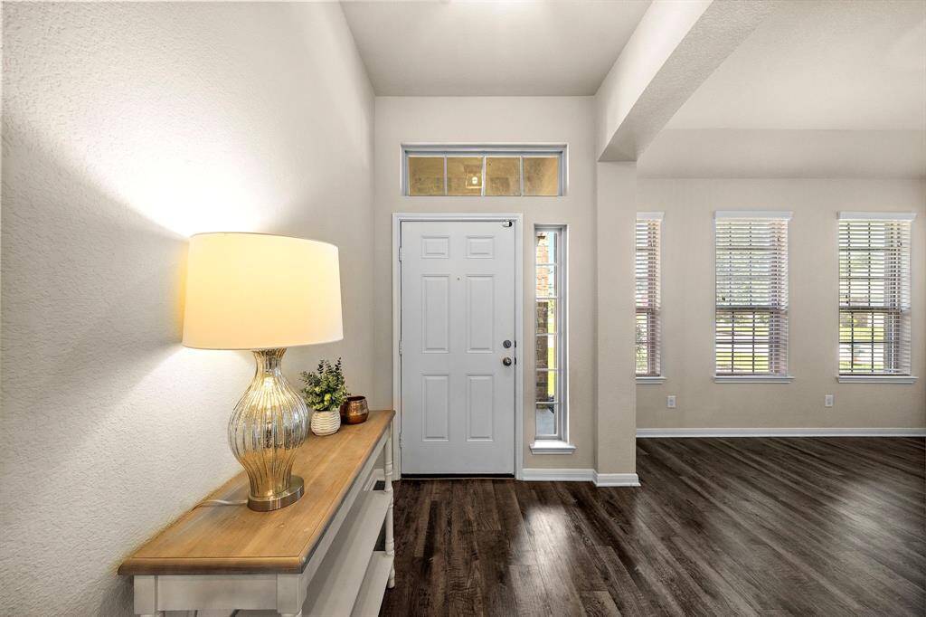 Natural light pours through sidelights and transom windows, highlighting the inviting entryway’s wood-look flooring and crisp trim. A decorative accent table offers a welcoming touch, while the open transition into the living space showcases the home’s seamless flow and modern appeal.