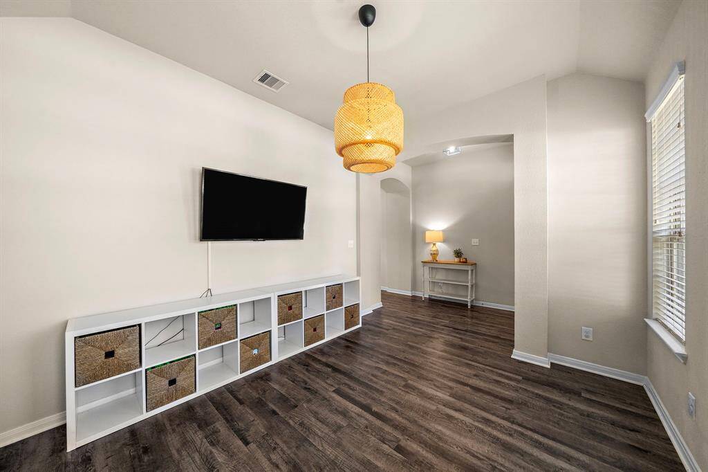 Versatile flex space offers the ideal spot for a cozy den or playroom, enhanced by a modern pendant light and built-in shelving. Wood-look flooring, a large window, and an arched entryway provide both style and functionality, making this room adaptable for everyday living.