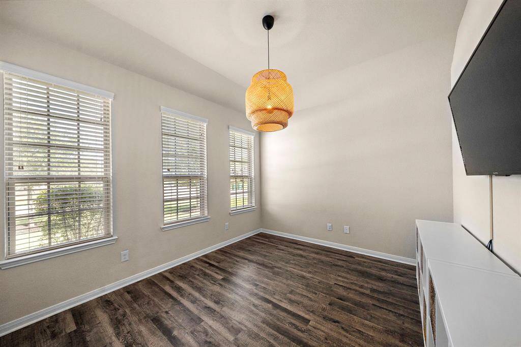 Abundant natural light fills this flex space through three oversized windows, while wood-look flooring adds warmth and durability. A striking woven pendant fixture centers the room, making it ideal for a home office, reading nook, or creative studio with open views of the landscaped corner lot.
