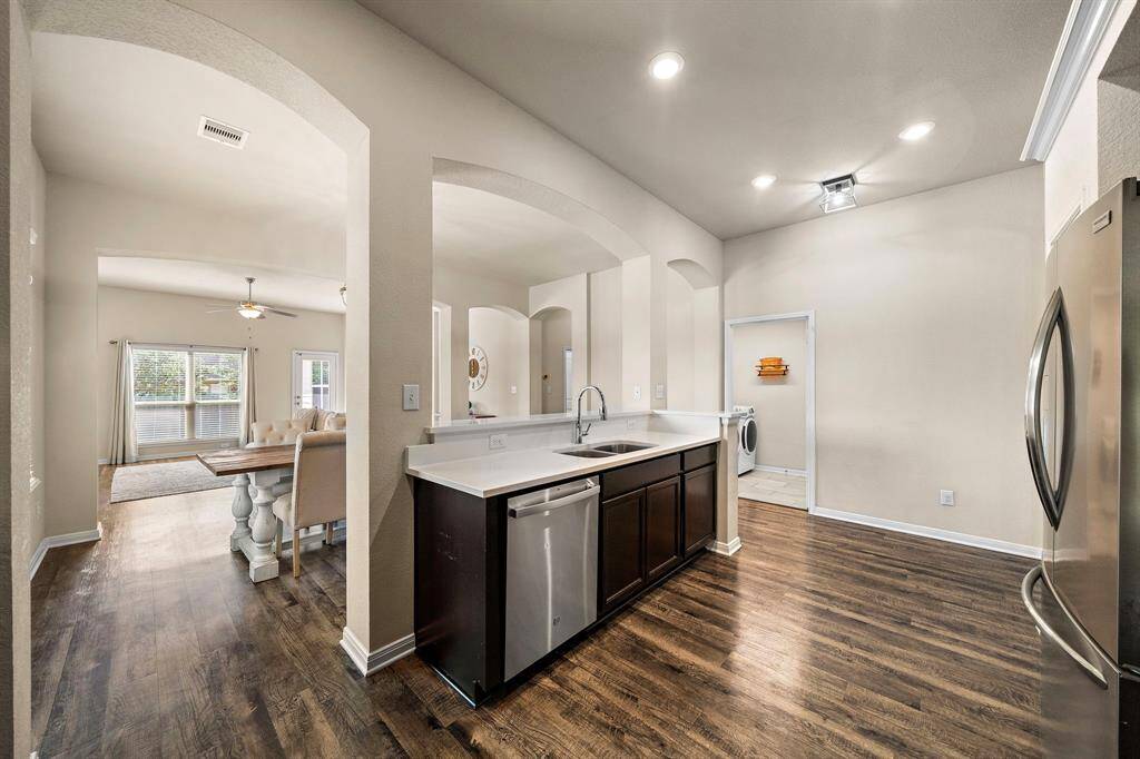 Open kitchen layout features a long breakfast bar with quartz countertops, sleek stainless steel appliances, and dark cabinetry for abundant storage. Conveniently connects to the laundry room and flows into a spacious dining area, making meal prep and gatherings seamless.