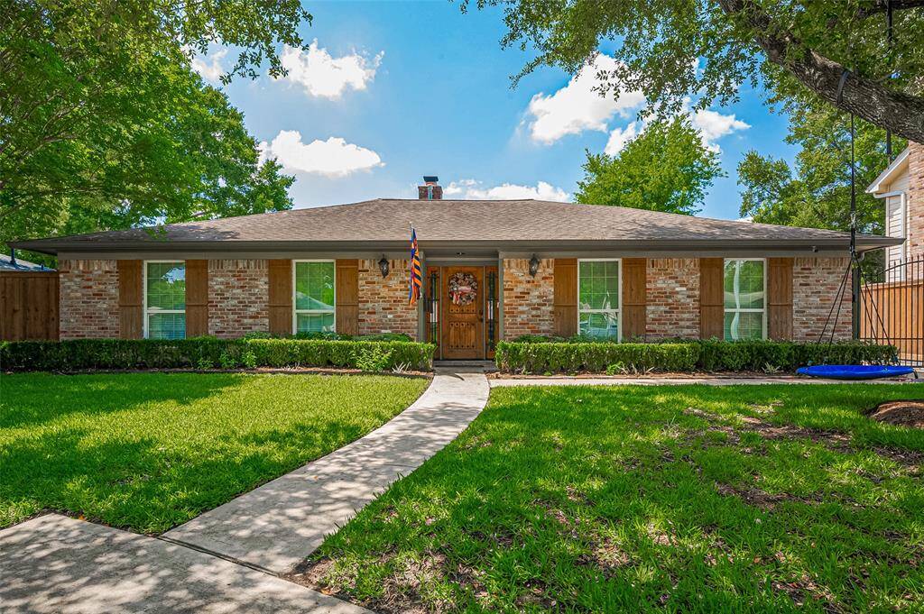 Charming one-story brick home on tree lined cul de sac street with a welcoming front walkway, nestled in a lush, well-manicured lawn. Features large windows, wooden shutters, and mature trees enhancing curb appeal.