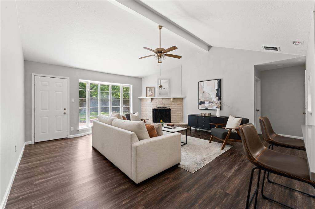 A cozy corner fireplace provides a charming focal point. It is surrounded by a brick hearth. An oversized pane window overlooks the backyard.