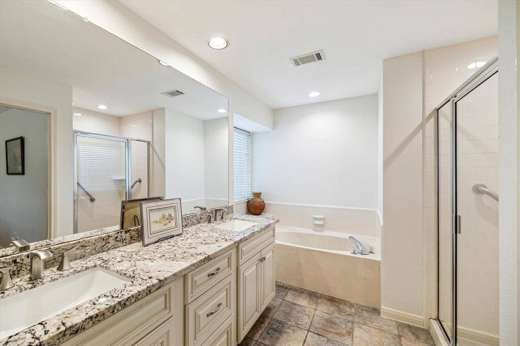 The updated en-suite primary bathroom features a double vanity with granite countertops, a glass-enclosed shower, and a separate bathtub.