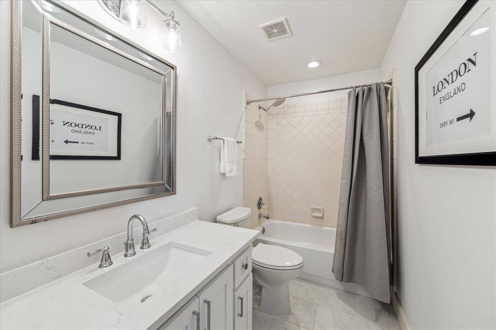 An expansive hall bathroom has a tub and shower.  A lot of cabinetry beneath the white sink and quartz countertop.  A medicine cabinet is integrated into the wall to the left of the mirror (not pictured).