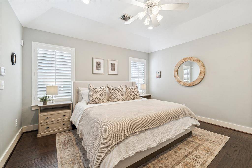 The luxurious primary suite have an angled tray ceiling, plantation shutters, recessed can lights, a ceiling fan with light kit, engineered wood floor, tall baseboards and a walk in closet.  An ensuite bathroom is to the right.