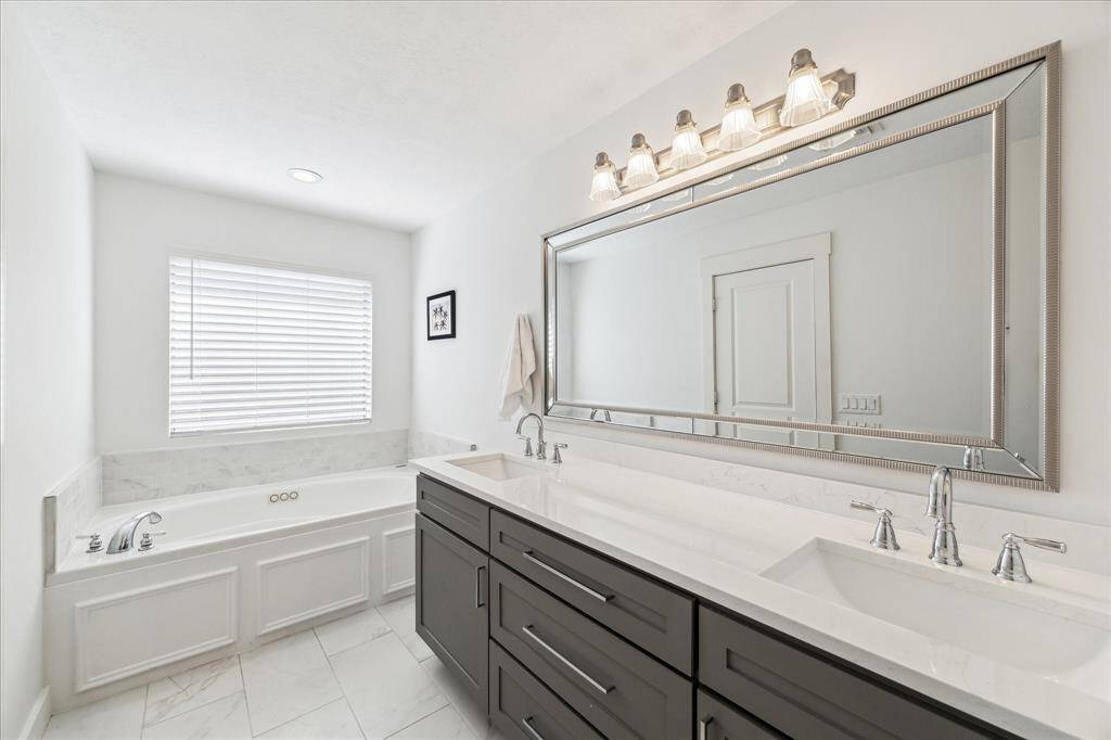 Another view of this pristine bathroom with abundant storage, double sinks, chrome fixtures, and large jetted bathtub. New tile flooring installed in 2021. Notice the beveled mirror above the quartz vanity and double sinks.