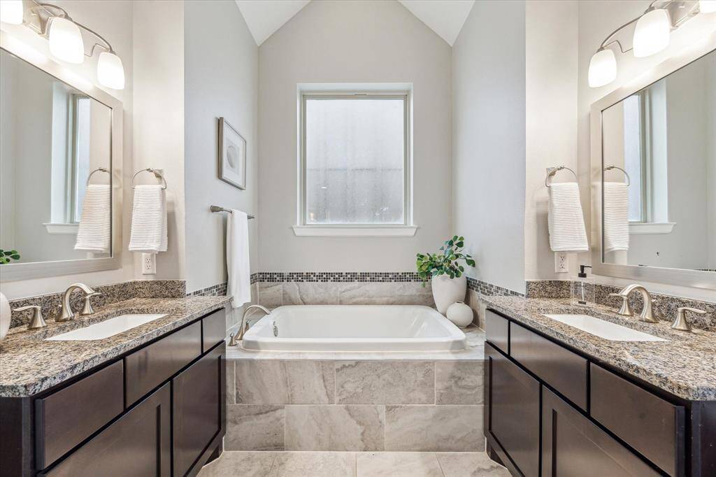 The luxurious primary bath showcases a 13-foot cathedral ceiling, dual vanities with granite countertops, a deep soaking tub, and a separate glass-enclosed shower.