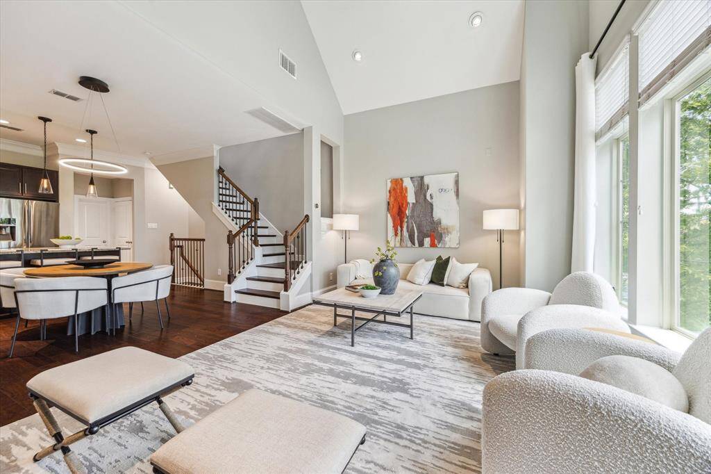 Stunning living area with tree top views through expansive windows, soaring 19-foot cathedral ceiling, rich accent wall, and recessed lighting that enhances the bright yet cozy ambiance.