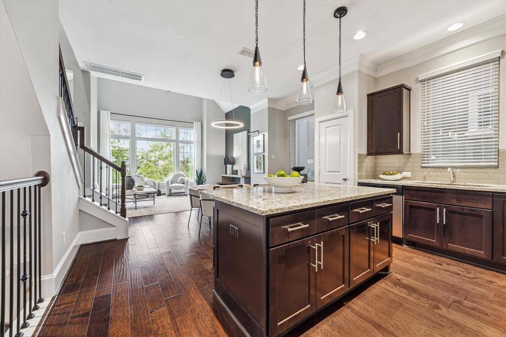 The chef-inspired kitchen features rich granite countertops, recessed lighting, abundant cabinetry, a large center island with breakfast bar seating, and triple glass pendant lights overhead.