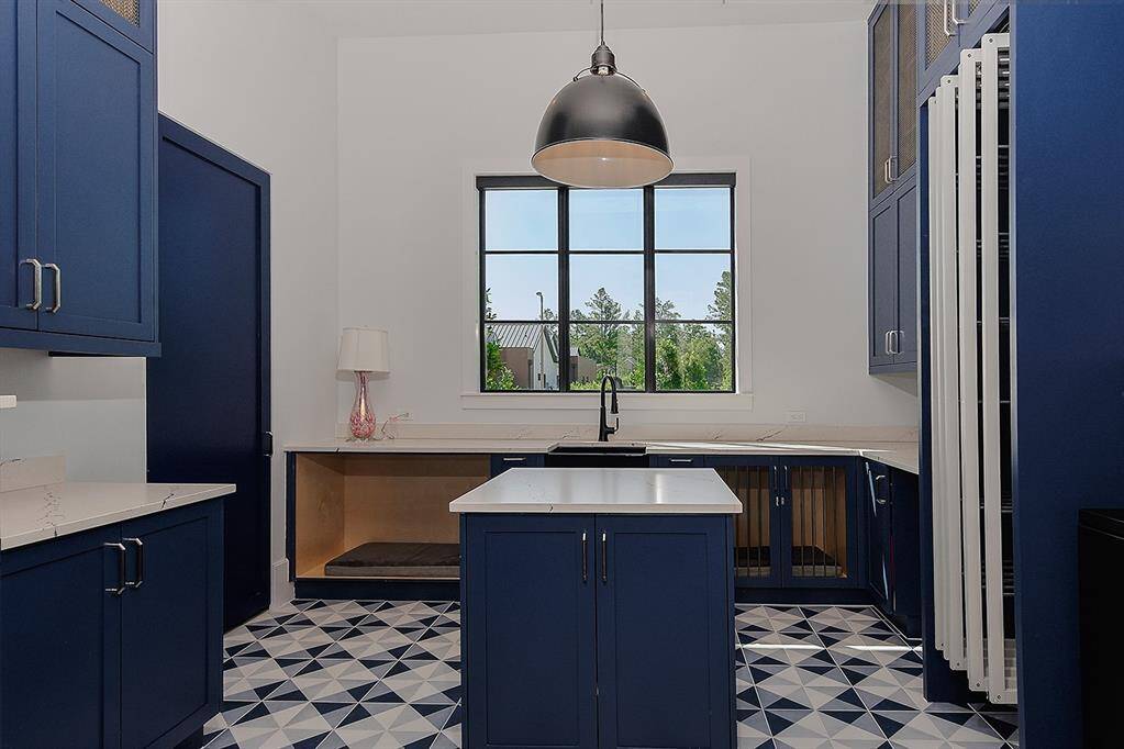 This downstairs laundry room offers a center island, built-in dog kennels, drying racks, abundant storage and quartz counters.