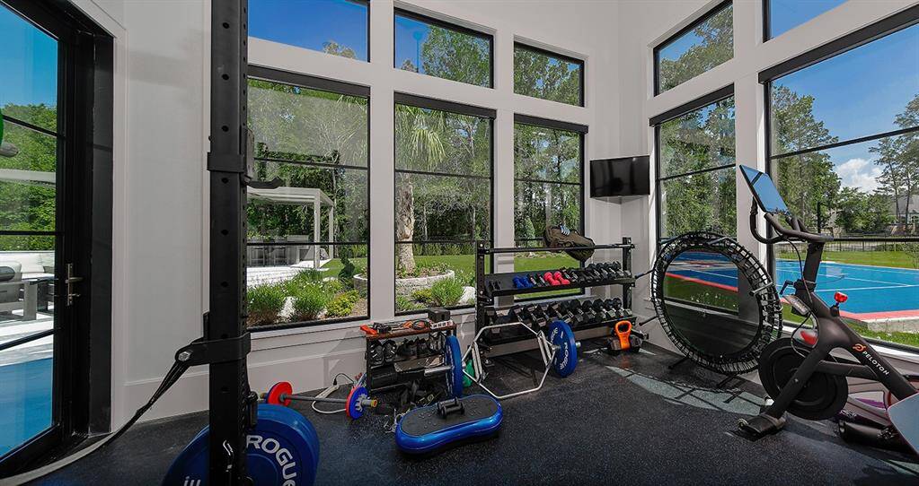 The fitness center off the primary suite is encased in windows, and has a door leading to the patio and pool.