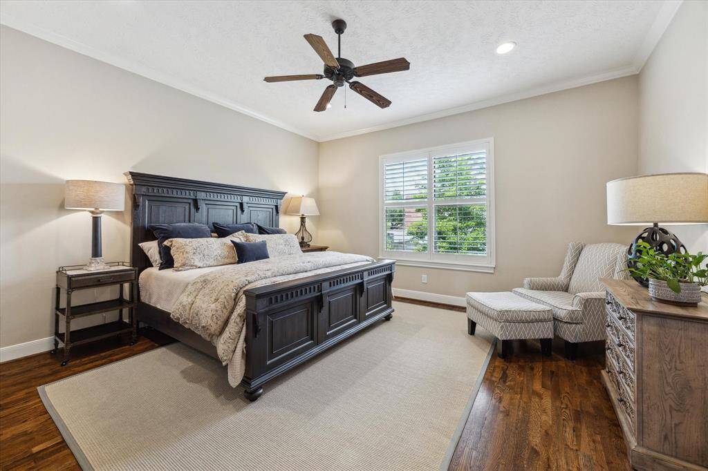 The spacious primary suite features rich hardwood floors, crown molding, and a large window with plantation shutters that flood the room with natural light.