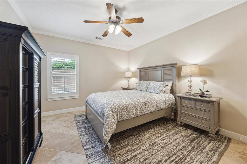 Spacious downstairs bedroom featuring neutral tones, crown molding, and a large window with plantation shutters—perfect for guests or multi-generational living.