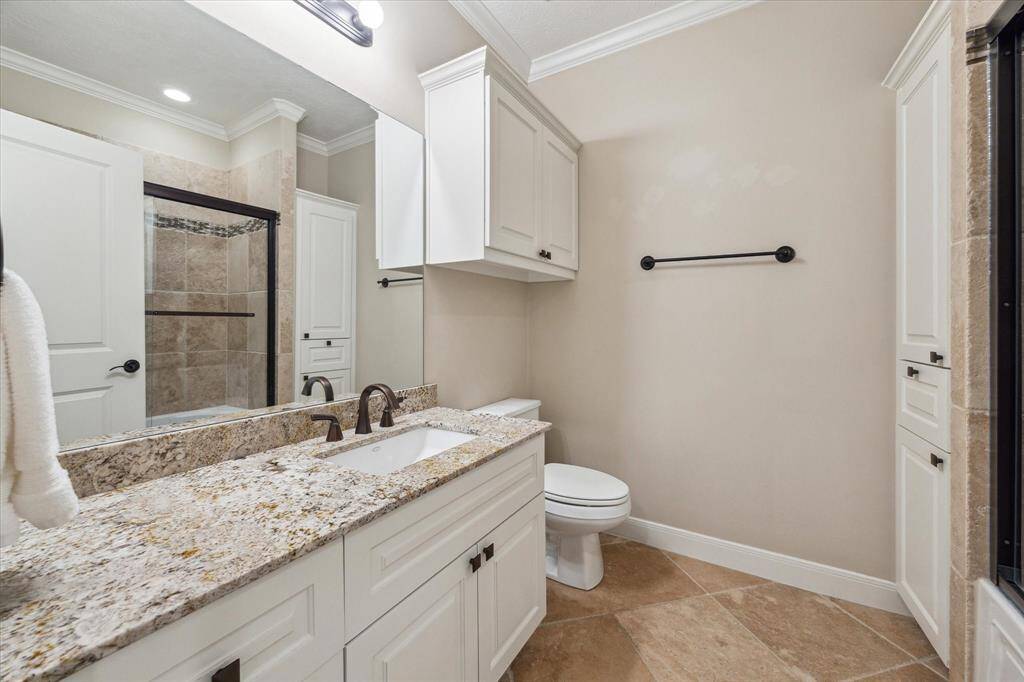 The secondary bath features a granite-topped vanity, oil-rubbed bronze fixtures, and a spacious walk-in shower with tile surround and built-in storage—both stylish and functional.