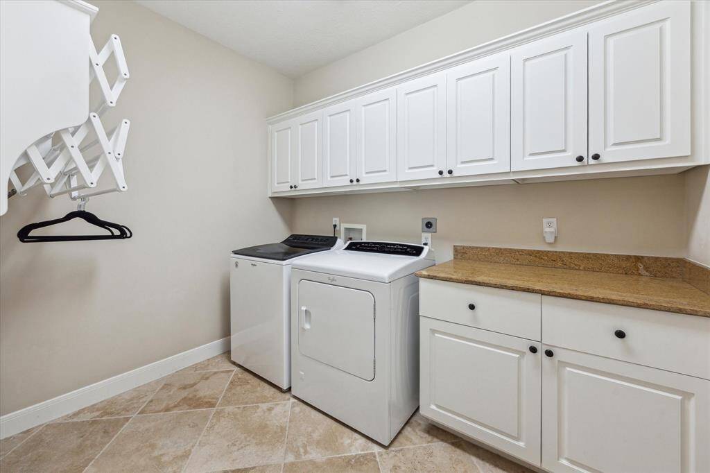A generously sized laundry room with upper and lower cabinetry, granite folding counter, and built-in drying racks—designed for efficiency and everyday ease.