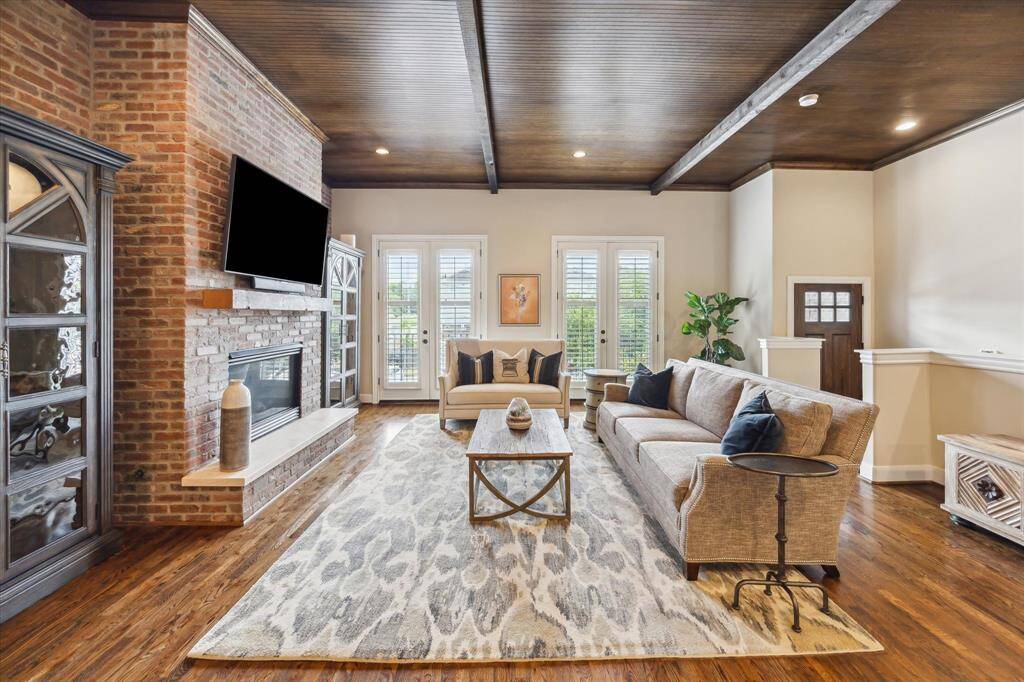 Cozy meets sophisticated in this spacious living room featuring a floor-to-ceiling brick fireplace, rich wood ceiling with beams, and double French doors that fill the space with natural light.