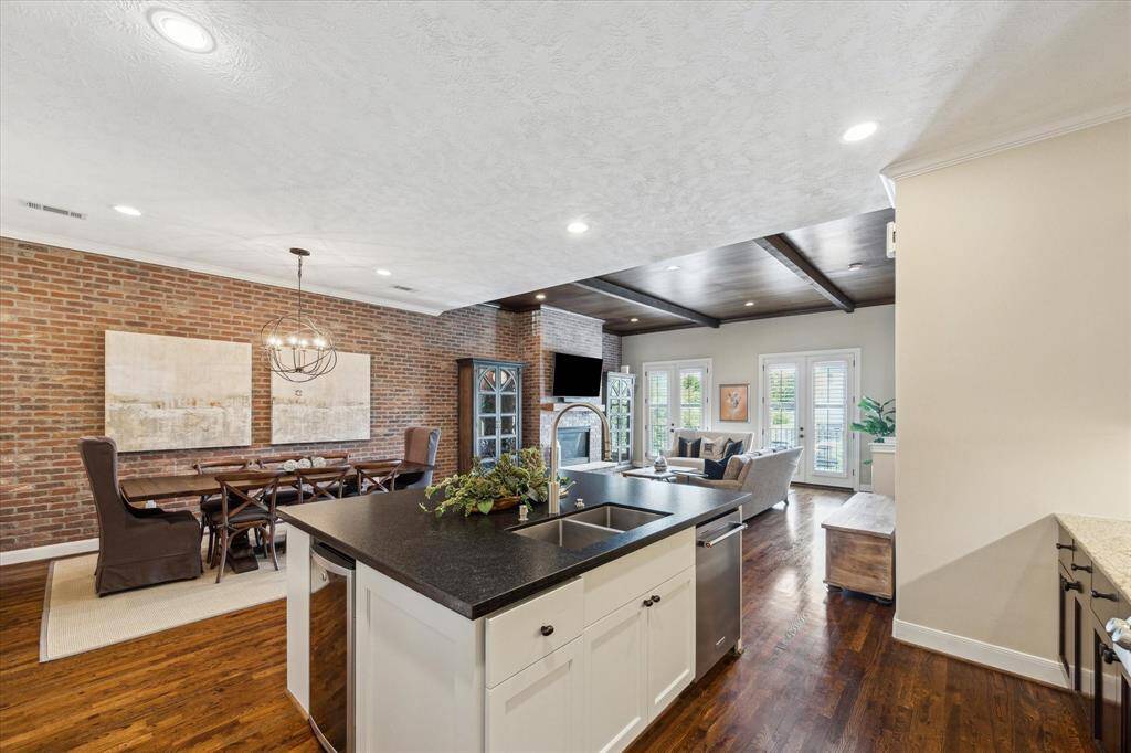 The seamless layout connects kitchen, dining, and living spaces—anchored by a large island with prep sink and views of the statement fireplace and double French doors.