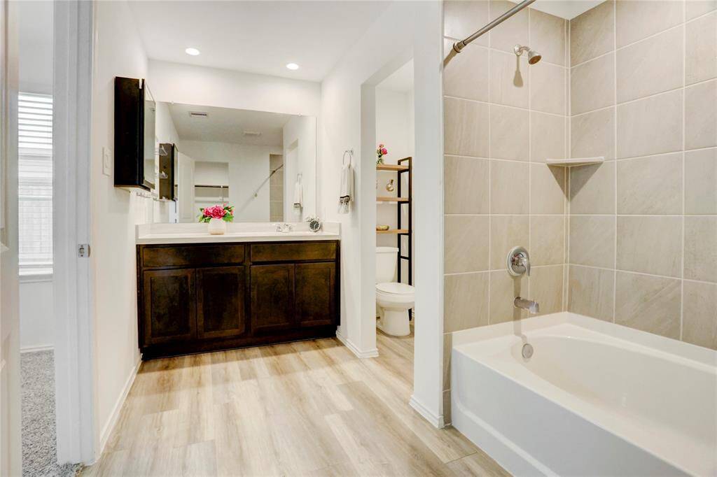 The primary en suite bath features a vanity with plenty of under-counter storage and a large mirror. A separate nook houses the water closet, with the shower-tub combo sitting adjacent.