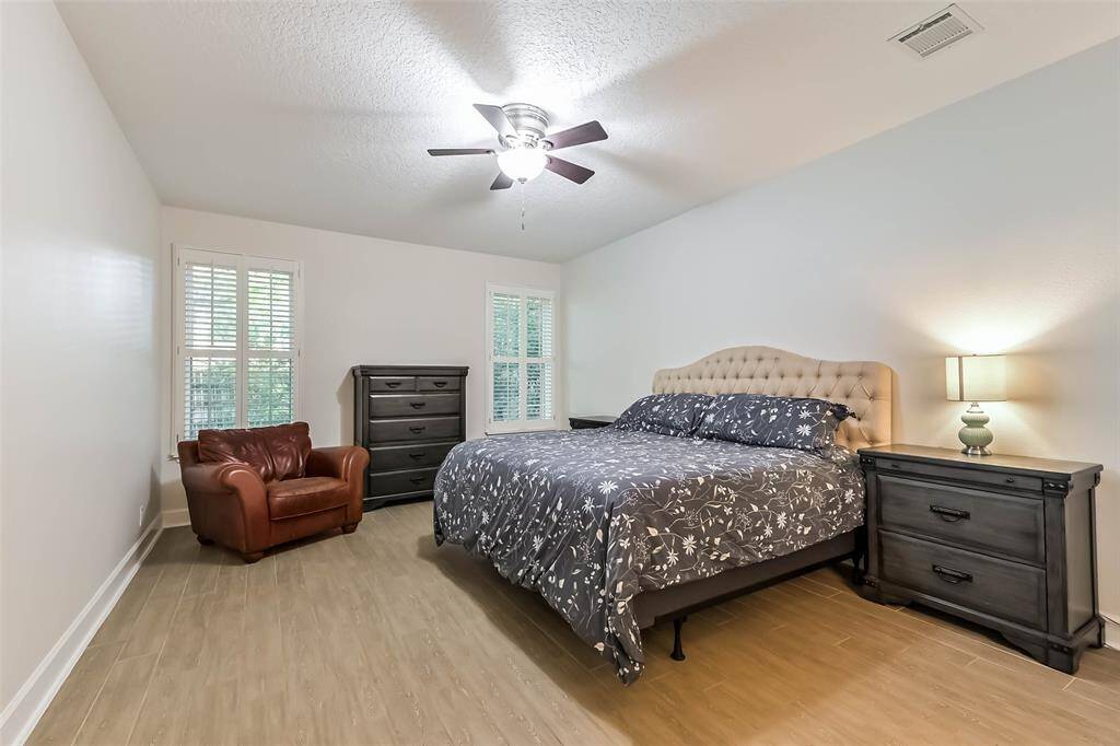 The primary suite is located on the first floor with a ceiling fan, wood like tile floors, and plantation shutters.