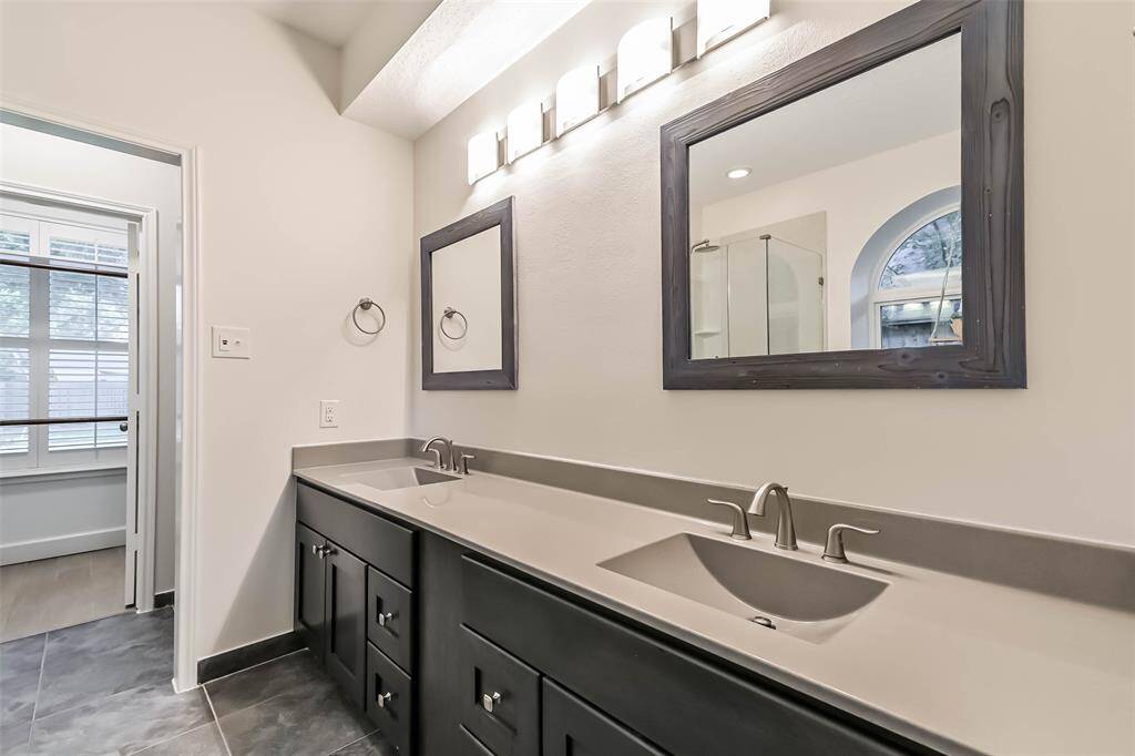 The primary bathroom features quartz counters, an updated vanity, double sinks, two framed mirrors, updated light fixture and tile floors.
