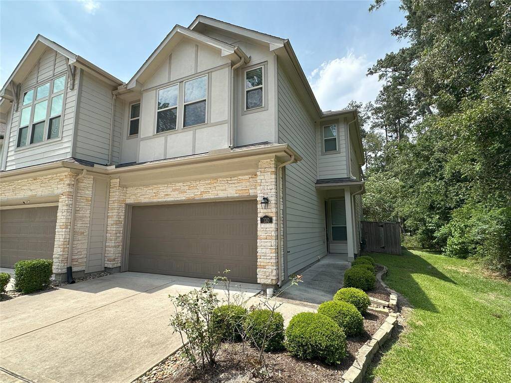 This is a modern two-story townhouse with a stone and siding exterior. It features a two-car garage, well-maintained landscaping, and a side pathway leading to a fenced backyard, offering both convenience and privacy.