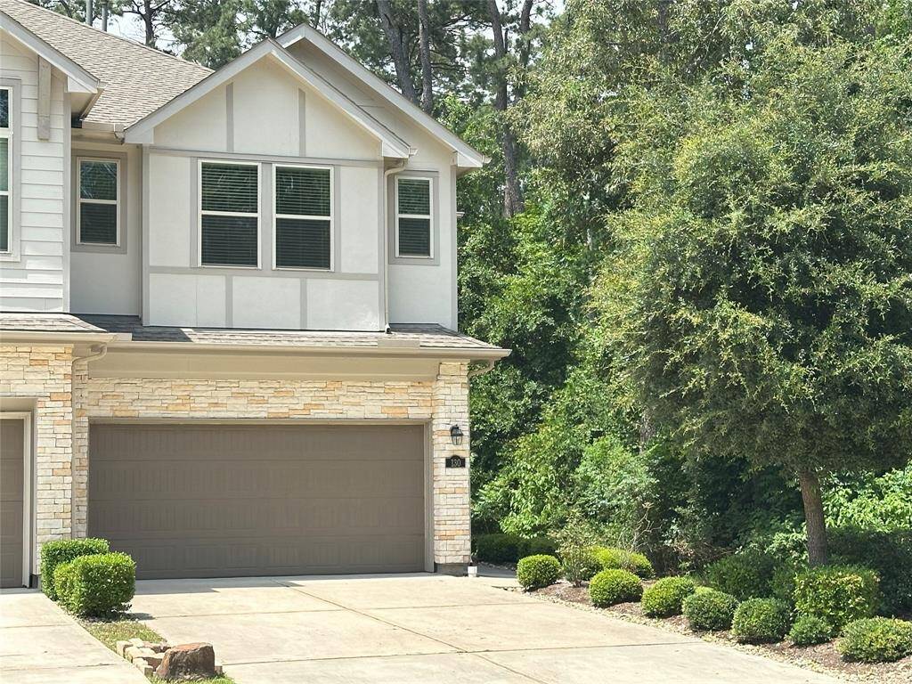 This photo shows a modern two-story home with a double garage, stone and siding exterior, and well-maintained landscaping. It's surrounded by lush greenery, providing a private and serene setting.