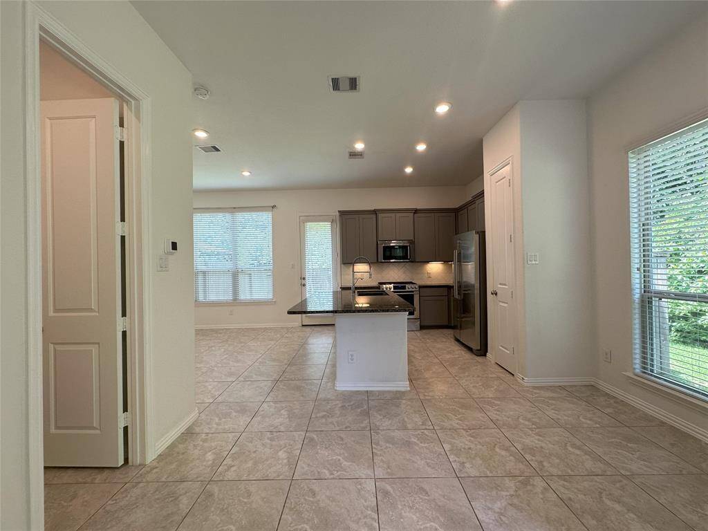 This open-concept kitchen features modern appliances, ample cabinetry, and a central island with a sink. It has large windows for natural light and connects seamlessly to the living area, offering a spacious and bright environment.