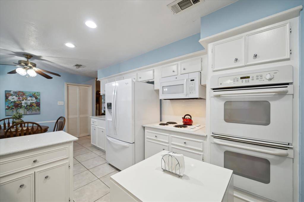 The open Kitchen boasts white appliances, white cabinetry, and tile flooring.