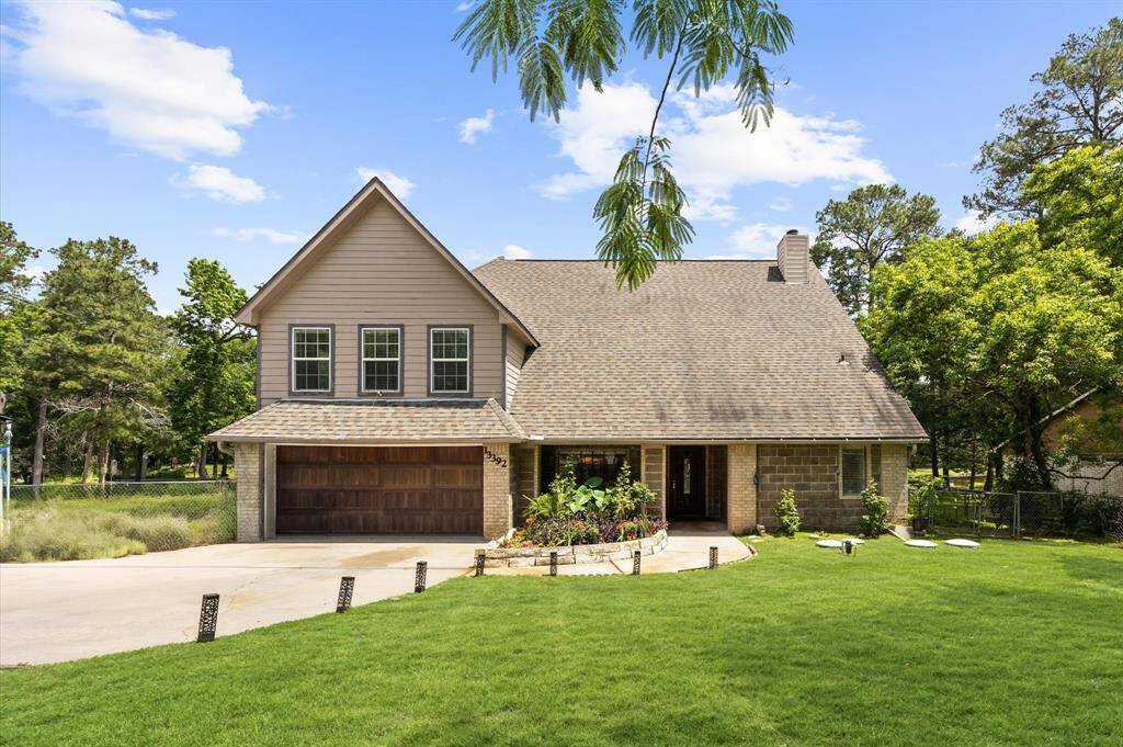 This charming two-story home features a gabled roof and a welcoming front porch. It has a spacious driveway leading to a two-car garage. The house is surrounded by lush greenery and mature trees, providing a serene and private setting.