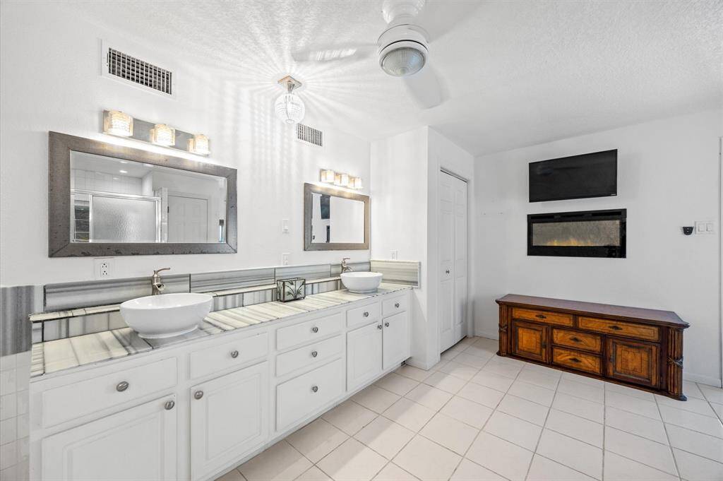 Luxurious primary bathroom with dual sinks, a cozy gas fireplace, and plenty of storage.