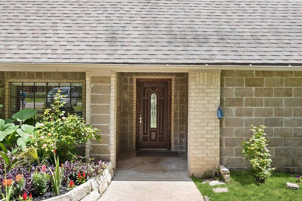 Home entrance with a detailed wooden door and decorative glass panel. The exterior features brickwork and a lush garden with vibrant flowers, creating an inviting atmosphere.