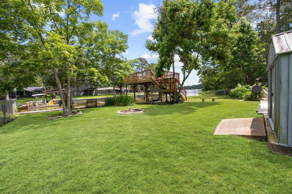Spacious lakeside yard with lush green grass, mature trees, and a wooden deck overlooking the water. Perfect for outdoor relaxation and entertaining.
