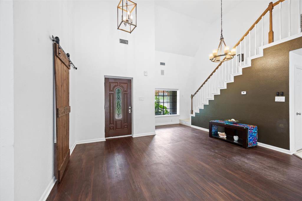 Bright entryway with high ceilings, featuring a wooden front door and sliding barn door. A modern chandelier adds elegance to the area.
