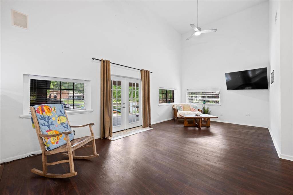 This spacious living room features high ceilings and abundant natural light. It includes French doors leading to pool and lake.