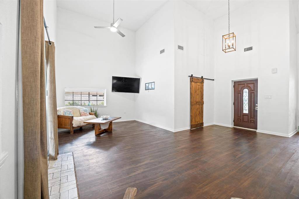 Experience spacious elegance with high ceilings, abundant natural light from the large window, and a cozy sitting area. A stylish barn door and charming front door complete the inviting atmosphere.