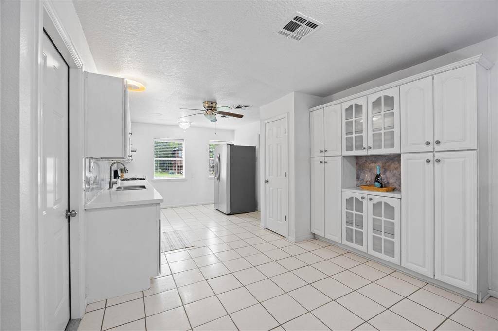 Bright kitchen with white cabinetry, ample storage, and tiled flooring. Features large windows for natural light.