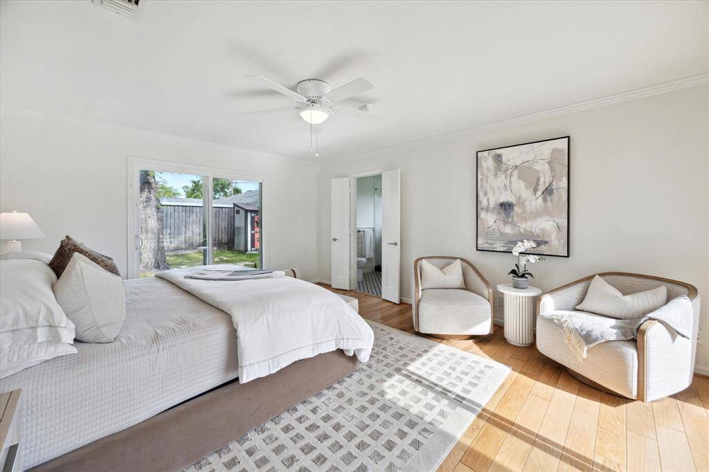 The primary suite showcases engineered hardwood floors, abundant natural light from two stunning floor-to-ceiling windows, and a ceiling fan with integrated lighting for added comfort.