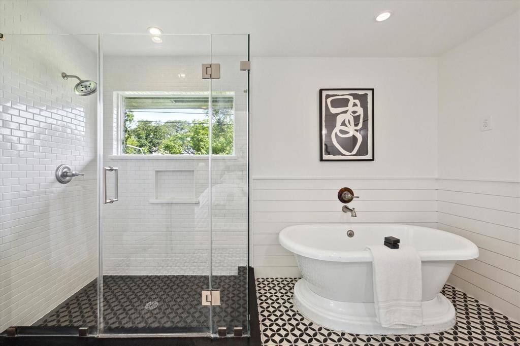 The ensuite bath was updated in 2017* and features a relaxing soaking tub, glass-enclosed shower, charming shiplap wainscoting, and stylish tile *per seller