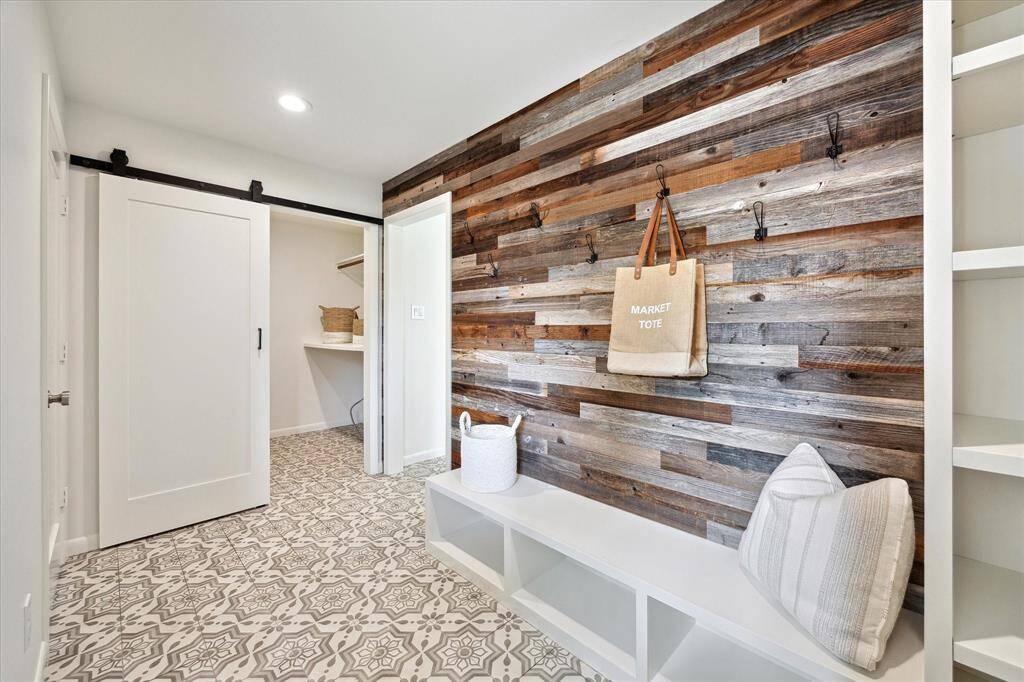 Conveniently located by the back door, the mudroom features a beautiful wood accent wall with hooks, a built-in bench with storage, and open shelving. It’s the perfect spot to drop your bags, shoes, and coats—keeping the rest of the home clutter-free.