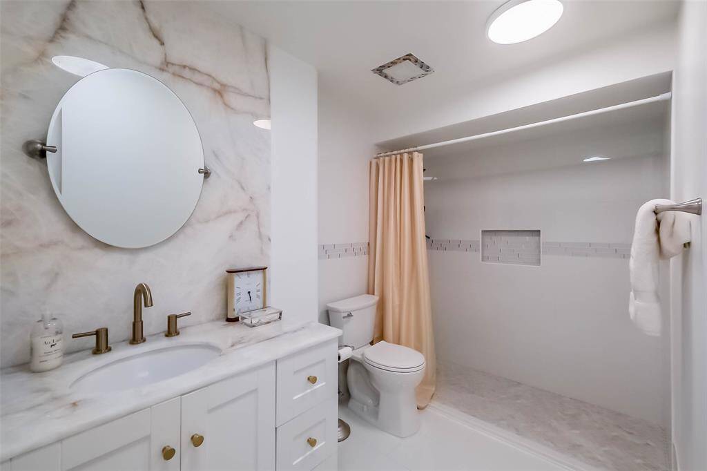 The beautifully updated primary bath includes a walk-in tiled shower and lighted quartzite backsplash and countertop.
