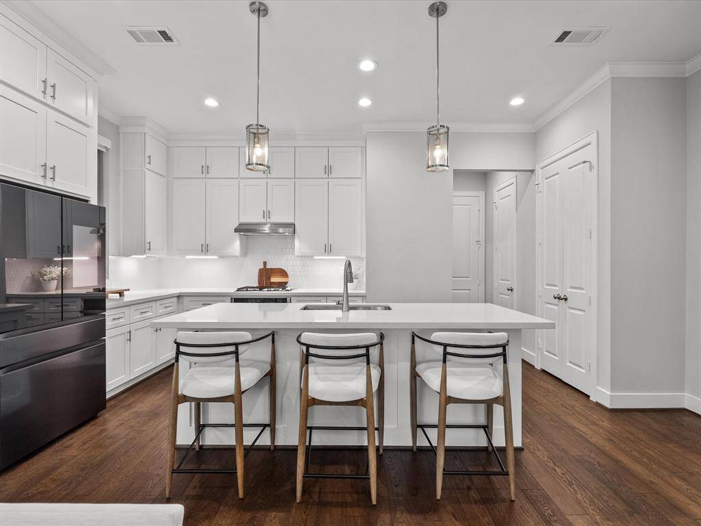 Modern kitchen features sleek white cabinetry, a large island, elegant pendant lighting, and high end stainless steel appliances.