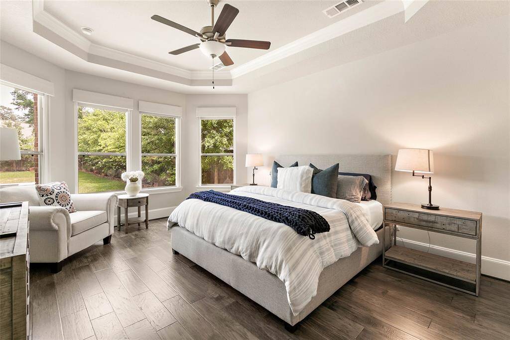 Spacious and elegant primary bedroom with tray ceiling and tranquil backyard views.  Enjoy the views during the day or sleep soundly with the convenience of electronic shades and black out blinds.