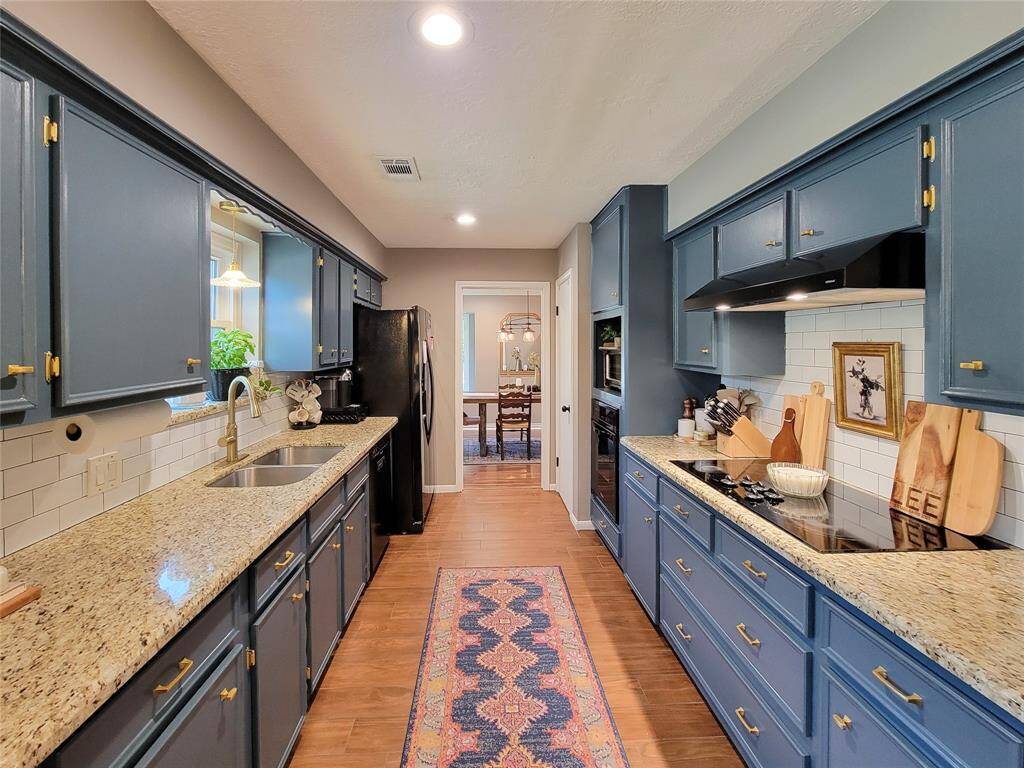 It includes a sleek cooktop, subway tile, wood-look tile flooring and all illuminated by recessed lighting.