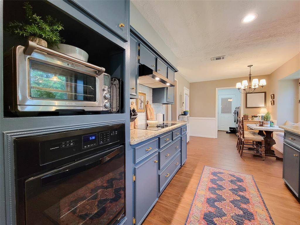 The space is well-lit with recessed lighting and a charming chandelier over the dining area. Warm wood-look tile flooring and a cozy dining nook create a welcoming atmosphere.