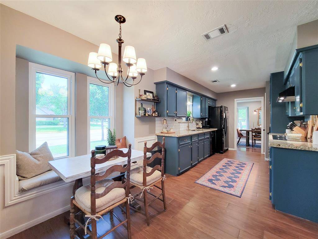 Bright kitchen with blue cabinets, granite countertops, and a cozy breakfast nook by a bay window. Features wood-look tile floors, modern lighting, and an adjacent dining area.